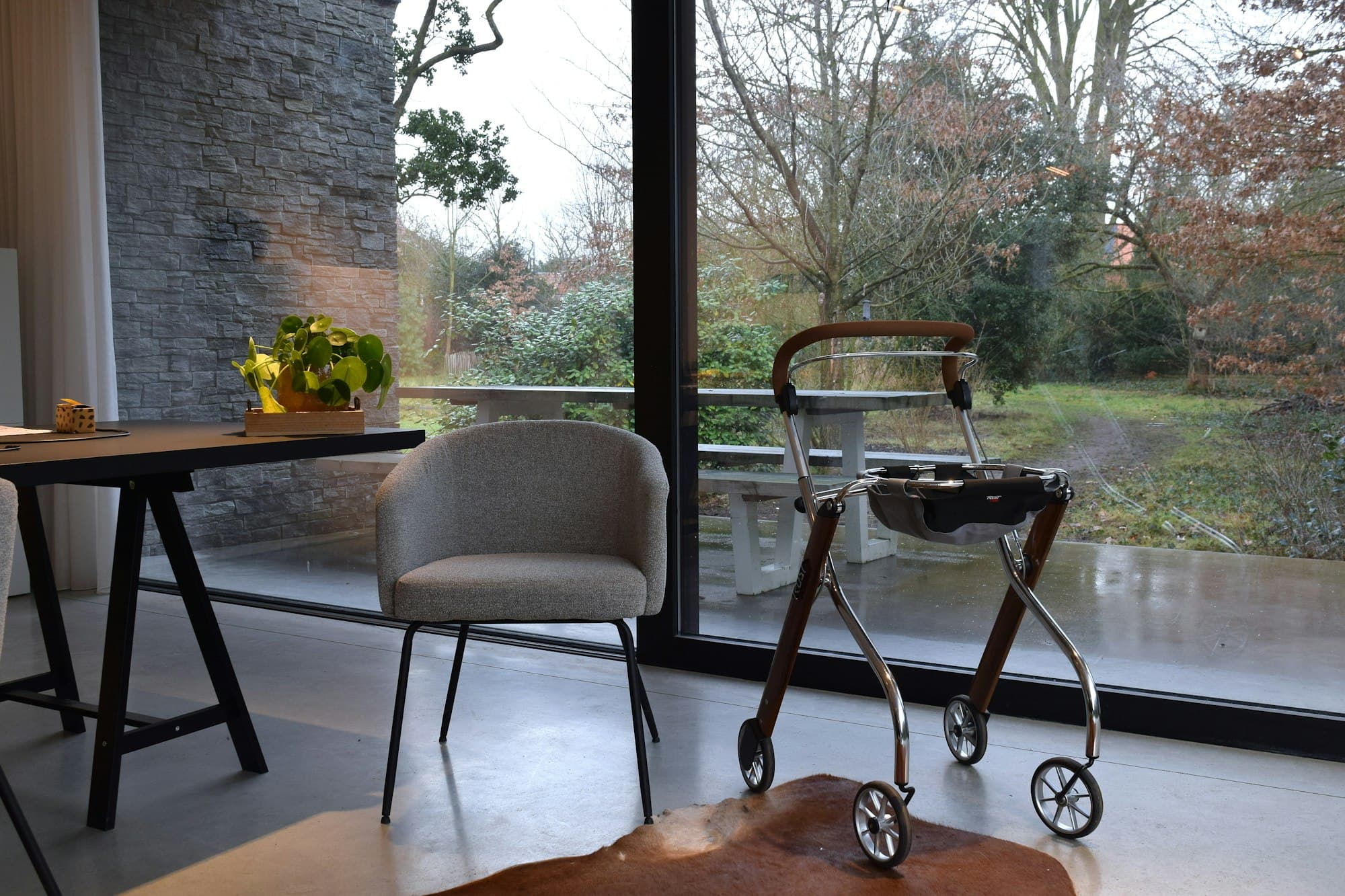 Un fauteuil et un déambulateur près d'une grande fenêtre donnant sur un jardin.